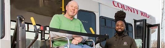 A man on a wheel chair being assisted off of a bus